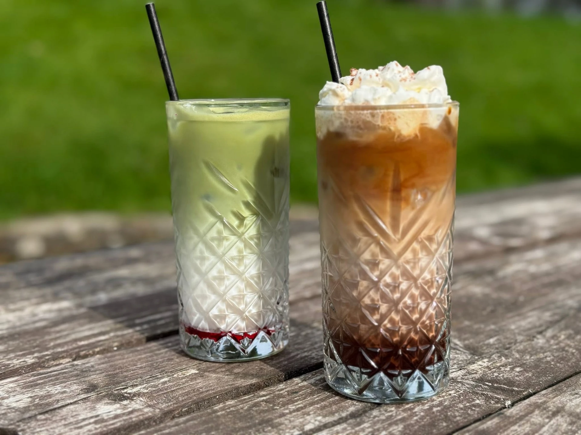 Two iced drinks in cut-glass tumblers on a wooden table outside
