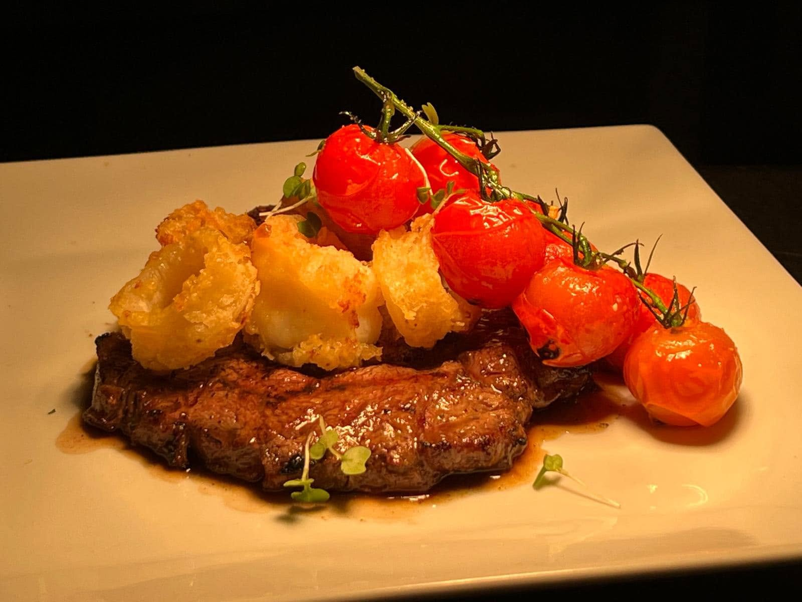 Steak served with vine tomatoes and crisp potatoes on a white plate