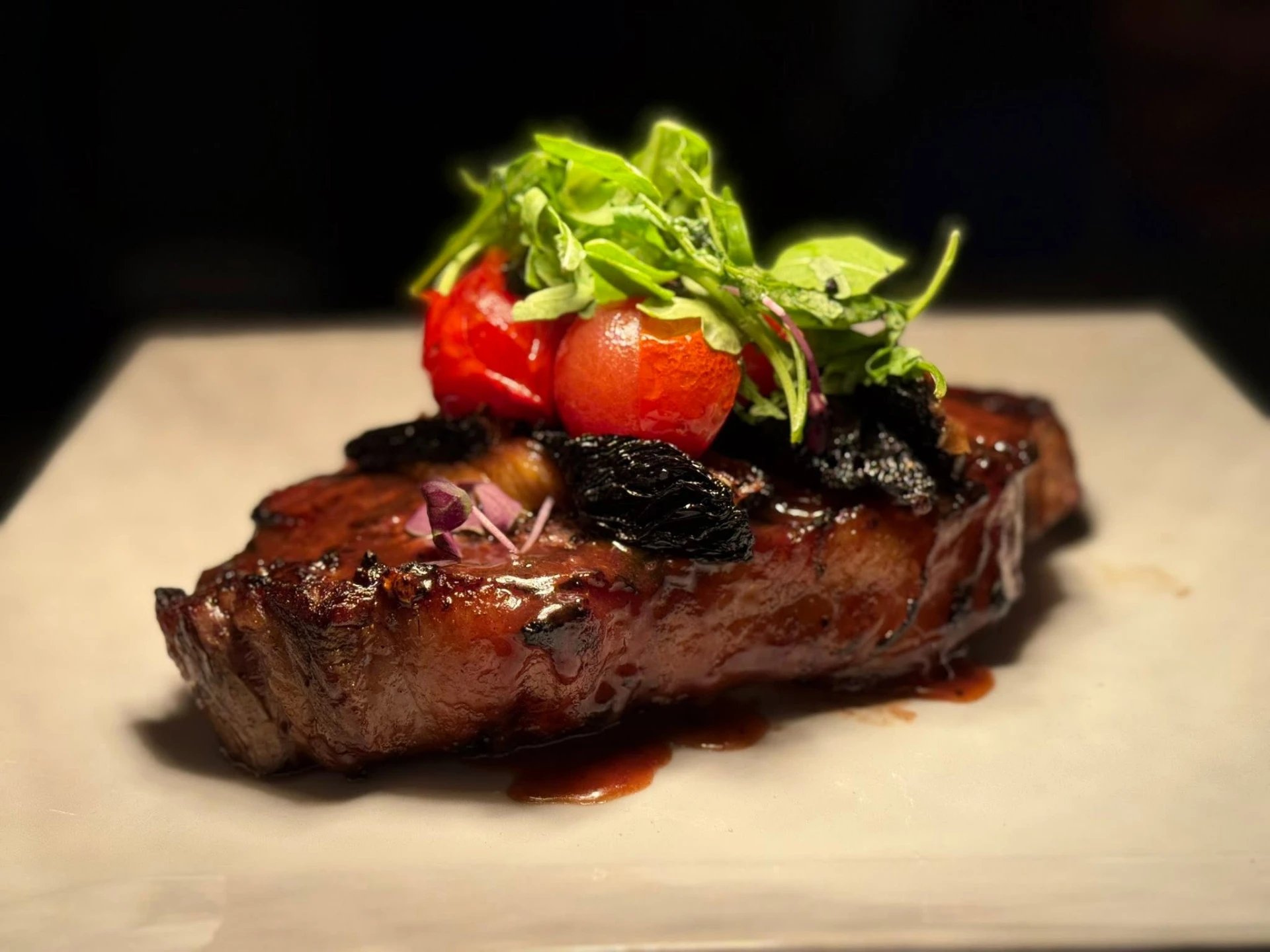 Close-up of a glazed steak with roasted tomatoes and fresh herbs