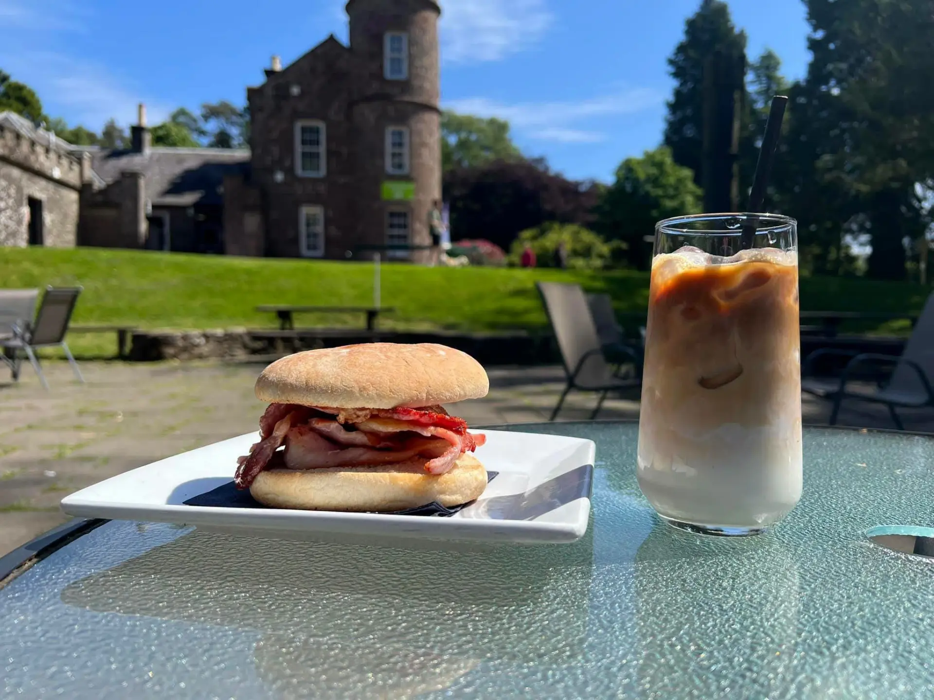 A bacon roll and iced latte on a terrace table with the café building behind