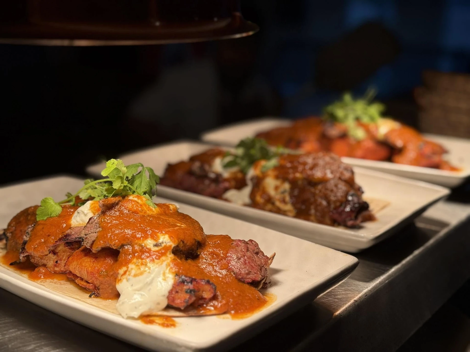 Plates of grilled meat with sauce and yoghurt lined up on the pass